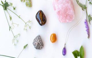 A selection of healing crystals including rose quartz, amethyst, pyrite, and tiger’s eye arranged with green leaves and flowers for karmic cleansing and balance.