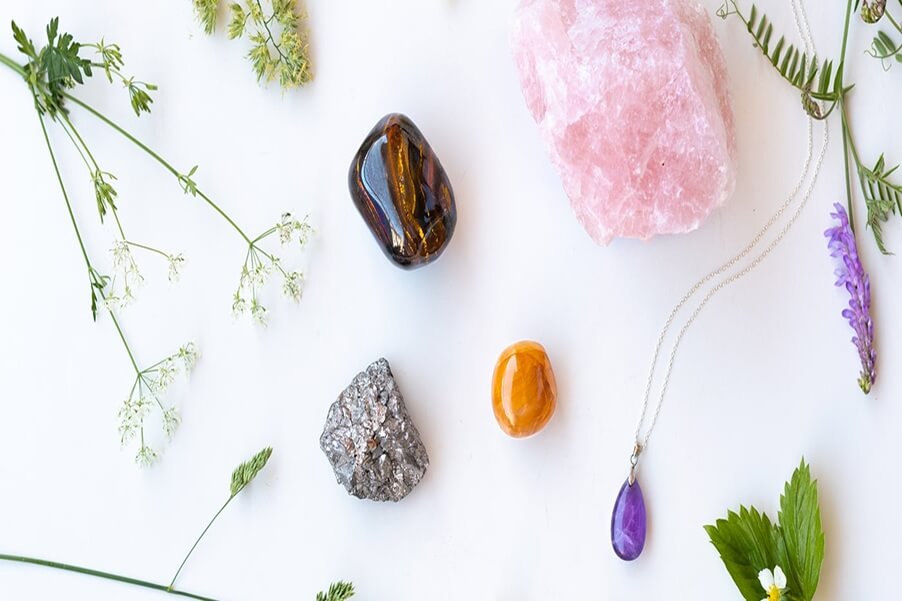 A selection of healing crystals including rose quartz, amethyst, pyrite, and tiger’s eye arranged with green leaves and flowers for karmic cleansing and balance.
