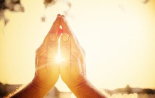 Hands in prayer position glowing with sunlight representing spiritual faith and inner belief