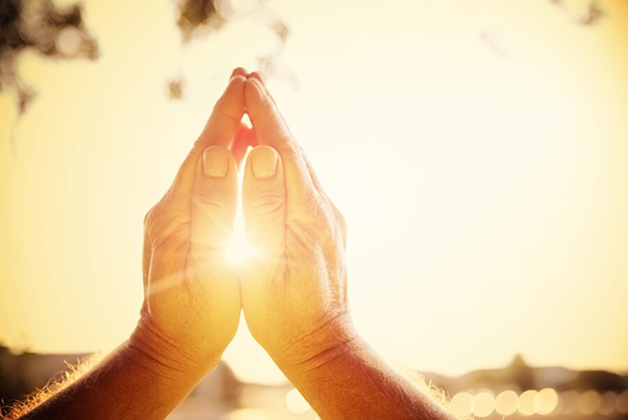 Hands in prayer position glowing with sunlight representing spiritual faith and inner belief