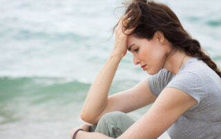 Woman sitting by the ocean looking worried, symbolizing how fear and anxiety pull us away from the present moment