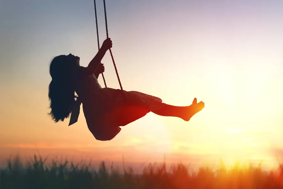 Silhouette of a young girl joyfully swinging at sunset, symbolizing freedom and emotional healing