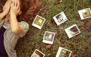 Woman covering her face surrounded by scattered photographs, symbolizing unresolved emotions and the need for past relationship closure.