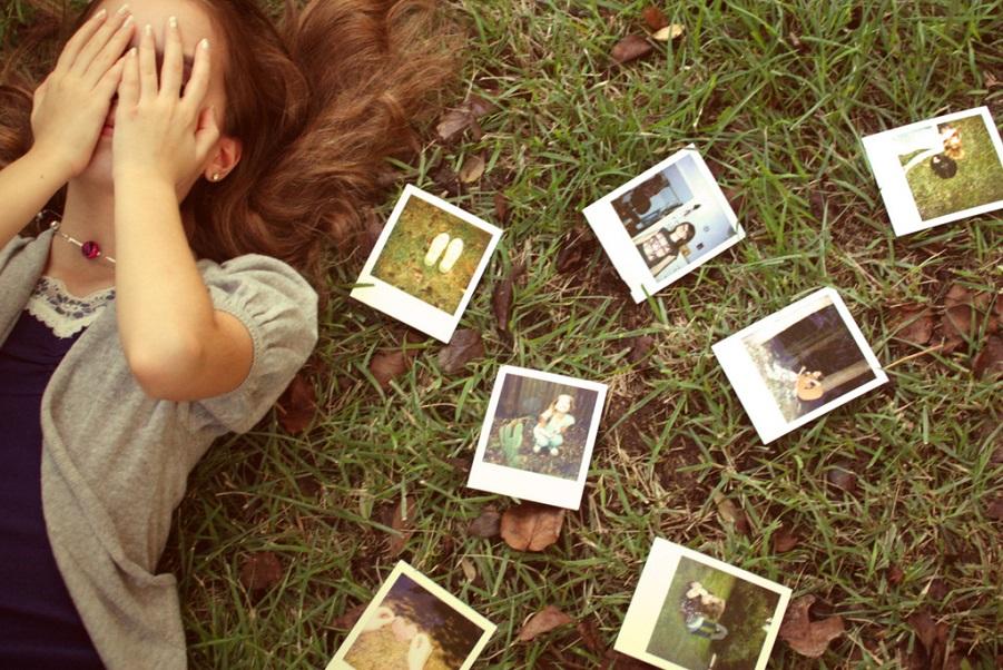 Woman covering her face surrounded by scattered photographs, symbolizing unresolved emotions and the need for past relationship closure.