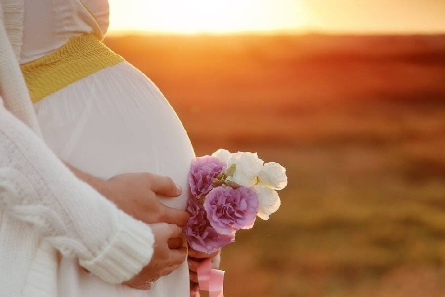 Pregnant woman holding flowers during sunset, symbolizing fertility and pregnancy psychic reading