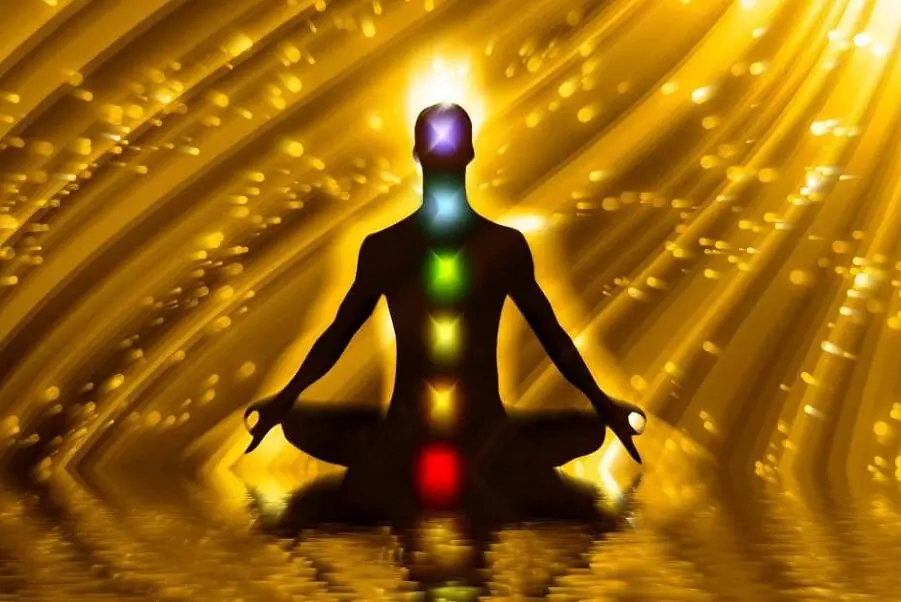 Silhouette meditating in golden light with illuminated chakras symbolizing the illumination of the luminous energy field through Shamanic Healing.