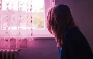 Woman looking out of a window in soft pink light