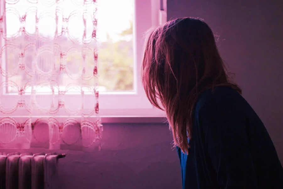Woman looking out of a window in soft pink light